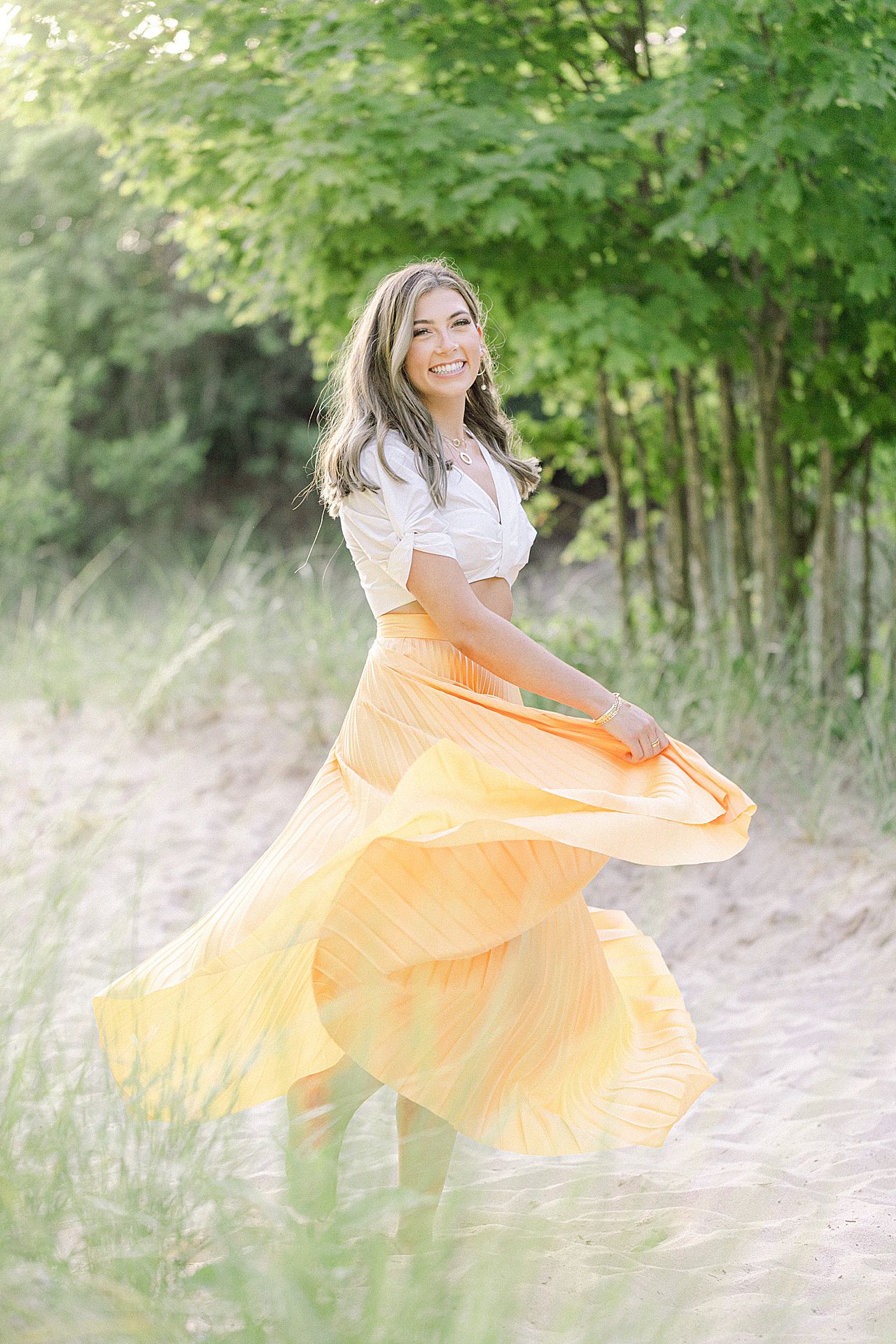 A portrait of a high school senior girl twirling her yellow flowing skirt on a sandy pathway in Michigan