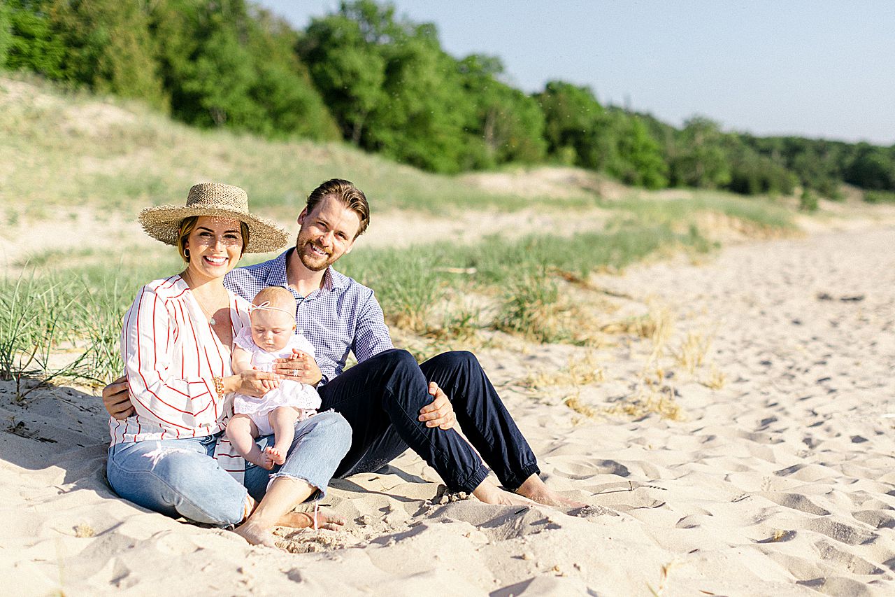 A mother and father sitting in the sand and holding their baby daughter in Northern Michigan