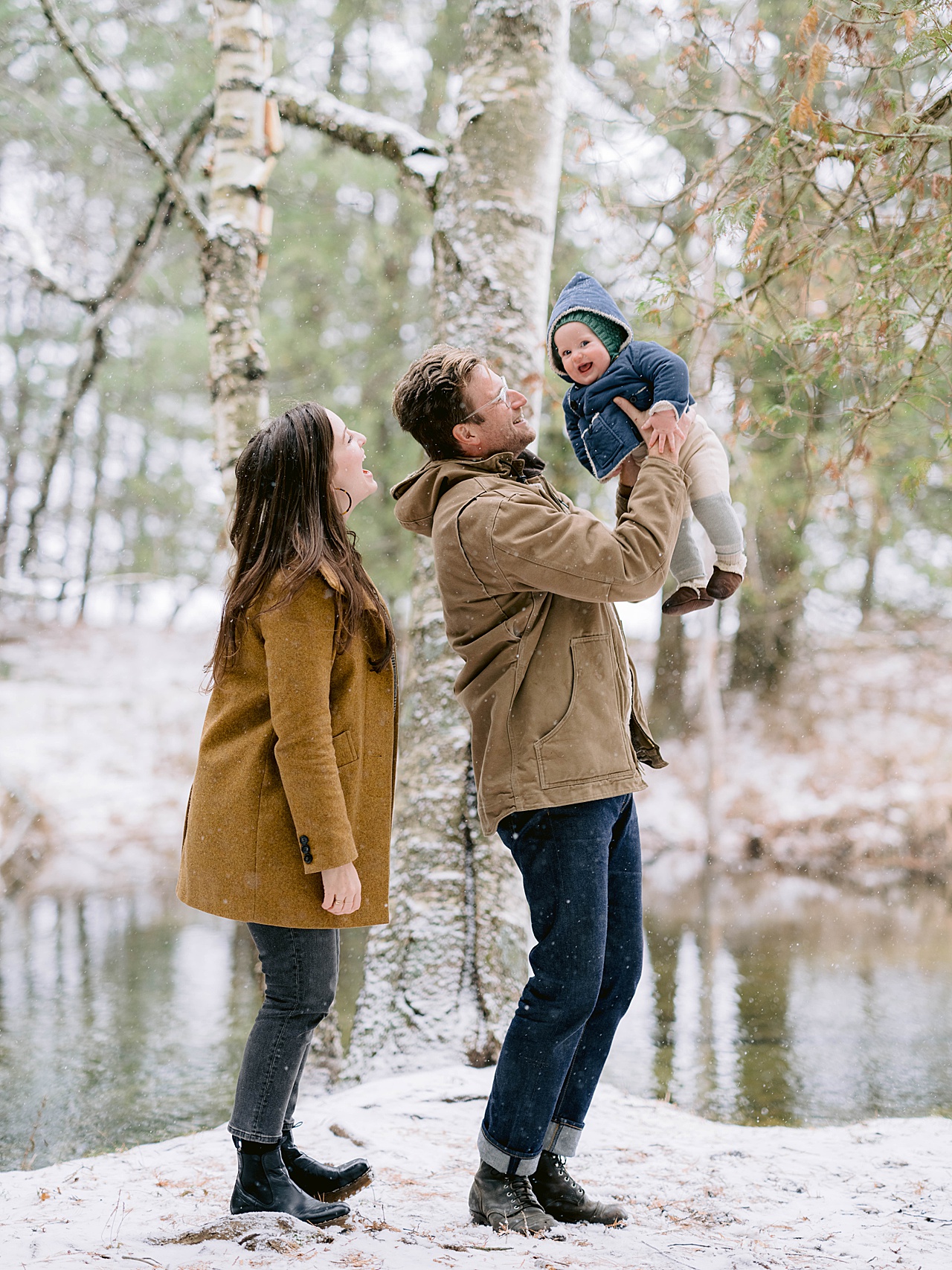 A baby laughing at the camera while playing with his parents