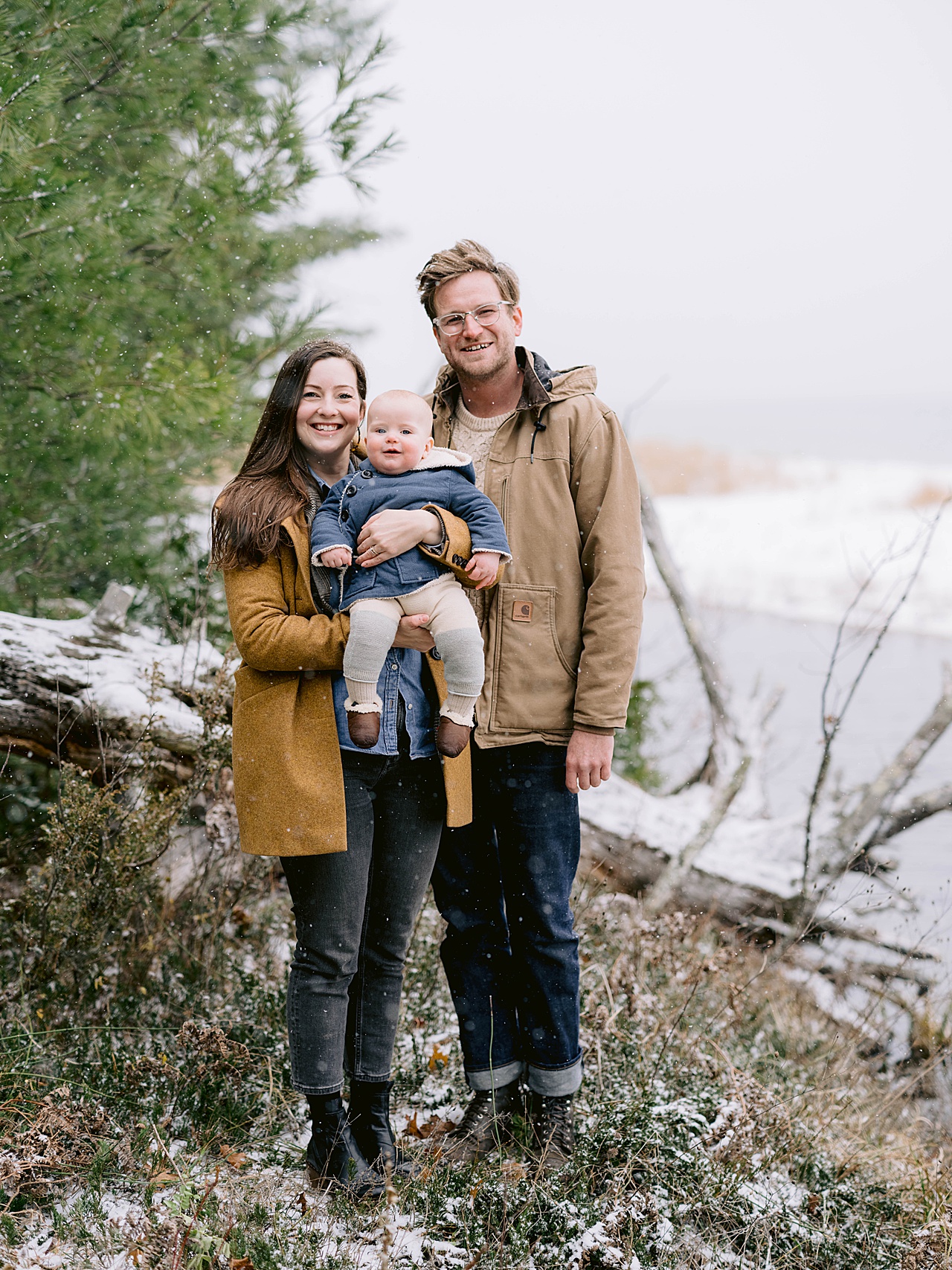 A mother, father, and baby smiling at the camera during their winter portrait session