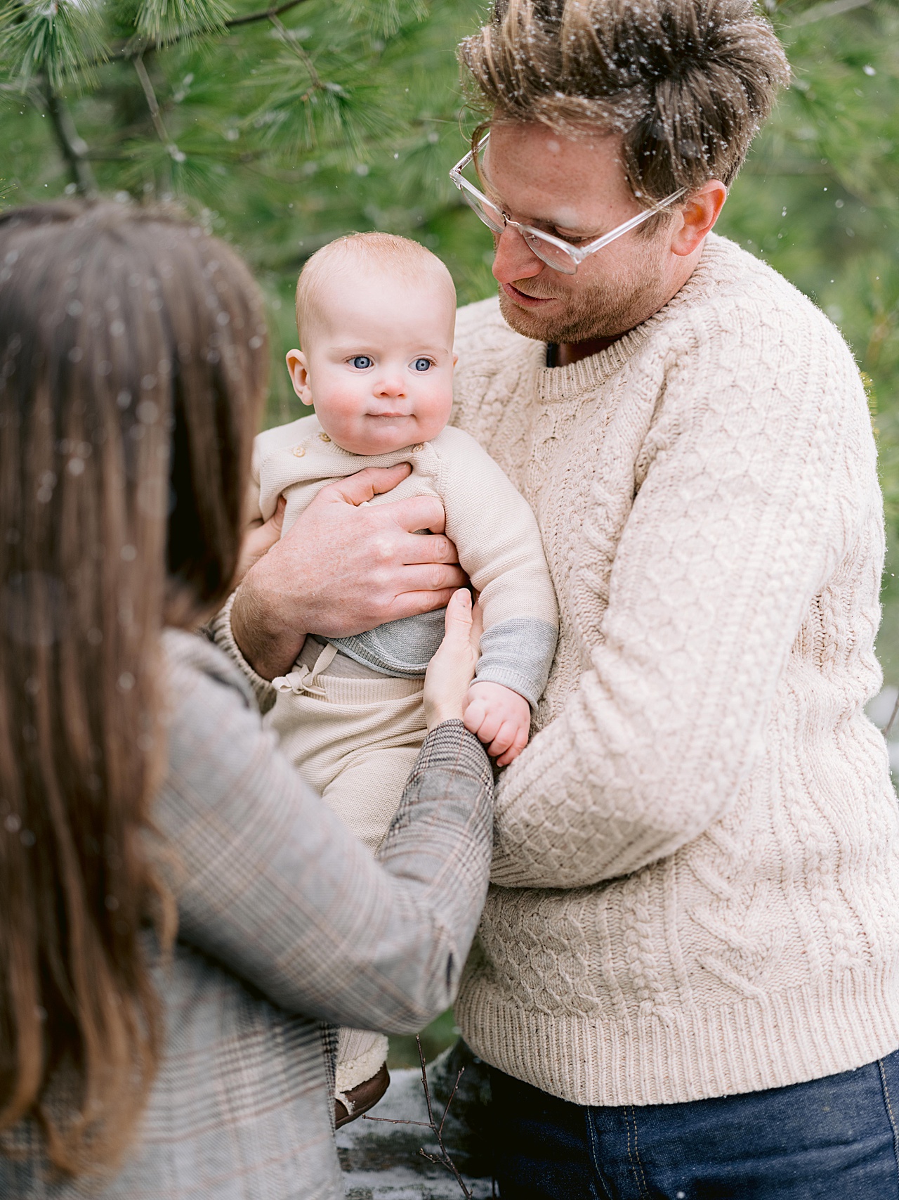A baby with bright blue eyes hanging out at a family portrait session in his dads arms