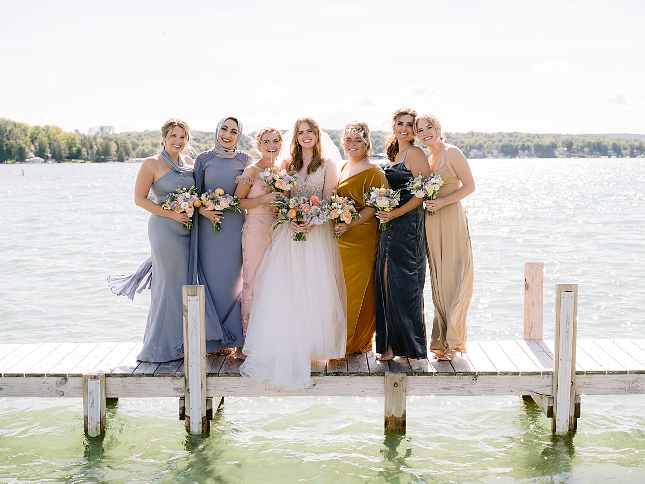 A bride and bridesmaids standing on a dock on a sunny day.