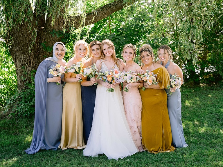A bride poses with her bridesmaids in the shade under a willow tree on Walloon Lake.