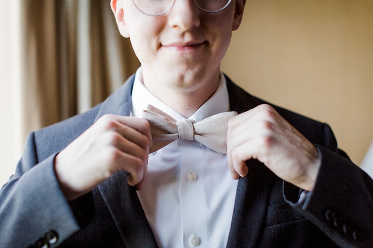 A closeup of a groom straightening his bow tie and smiling.