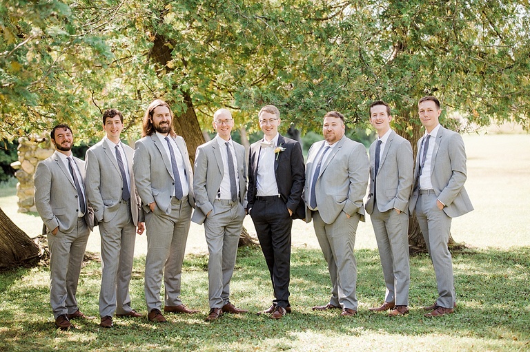 A stylish groom and groomsmen posing with hands in pockets under a tree in Michigan.