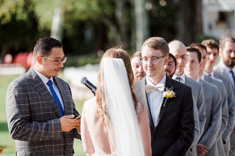 A groom smiling at the bride during the ceremony with groomsmen standing behind him.