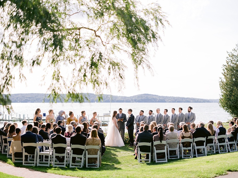 A wedding ceremony on a lake in the sunshine with a willow tree branch hanging overhead.
