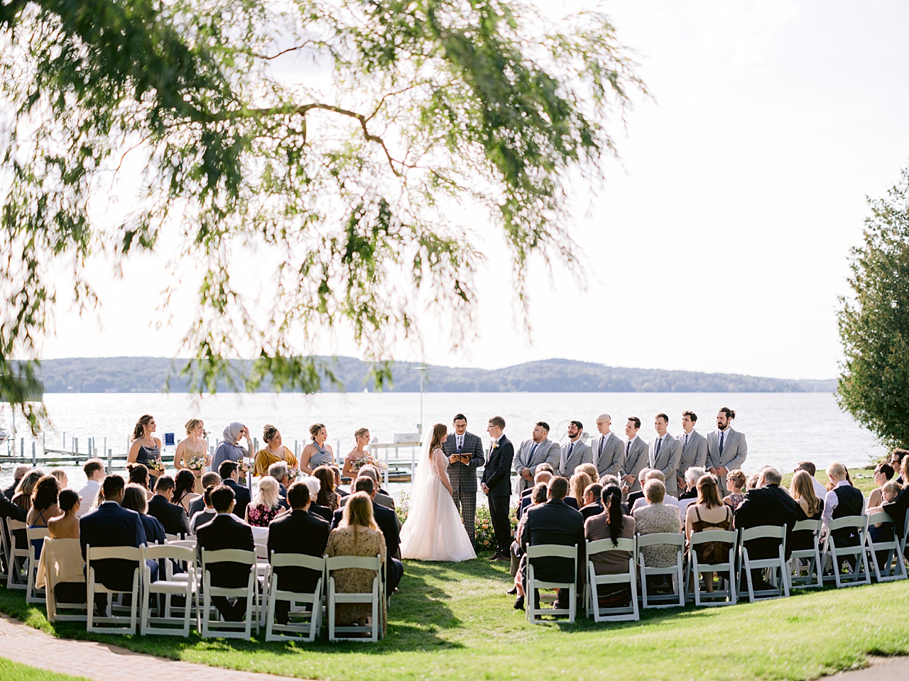 A wedding ceremony on a lake in the sunshine with a willow tree branch hanging overhead.