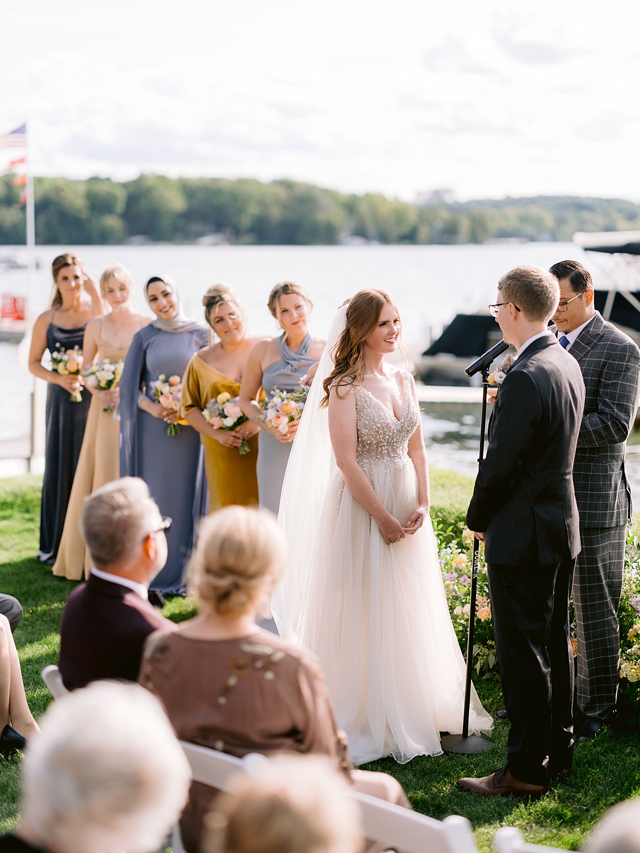 A bride and groom at a wedding ceremony smiling at each other with a line of smiling bridesmaids behind them.