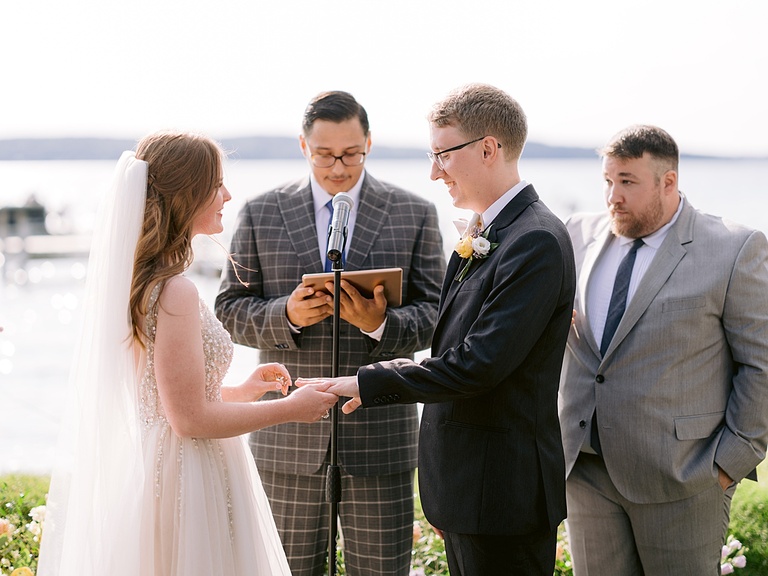 A bride and groom smiling and exchanging rings on a lake in Michigan.