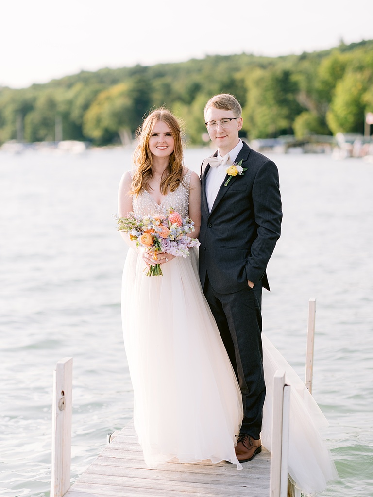 A bride and groom standing on a dock while the wind lightly blows bride's dress and hair.
