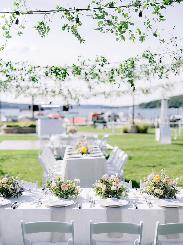 A reception on the lake with white wooden folding chairs and hanging lights.