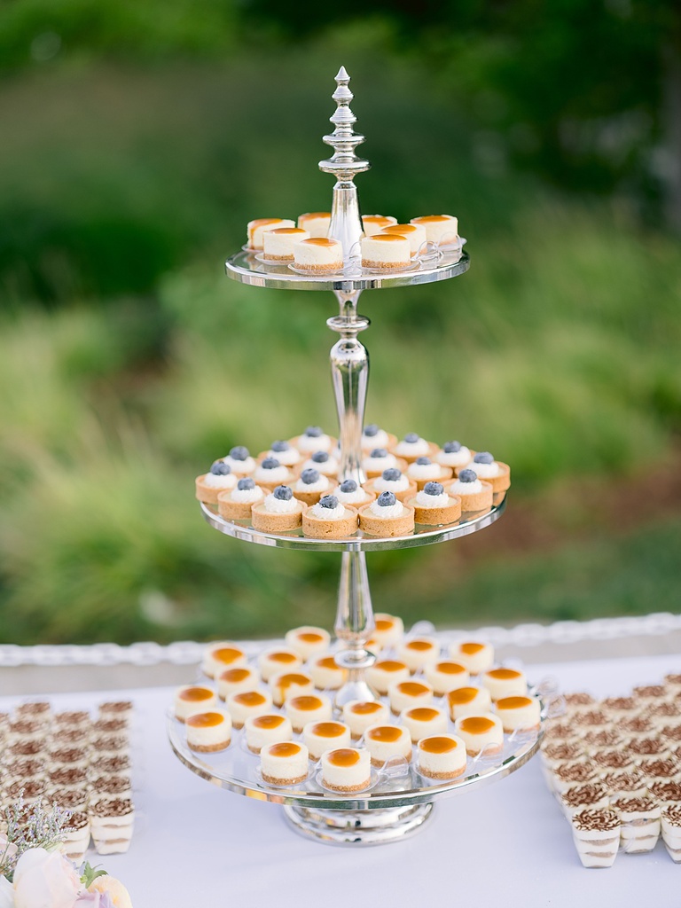 Desserts are displayed on a three tier cake stand with green, summer grass in the background.
