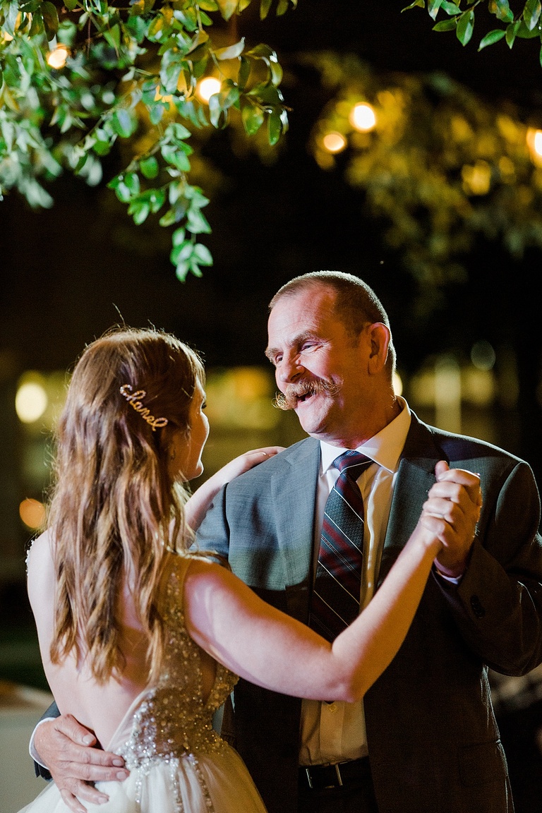 A bride's father singing to her under party lights and greenery during the father daughter dance.
