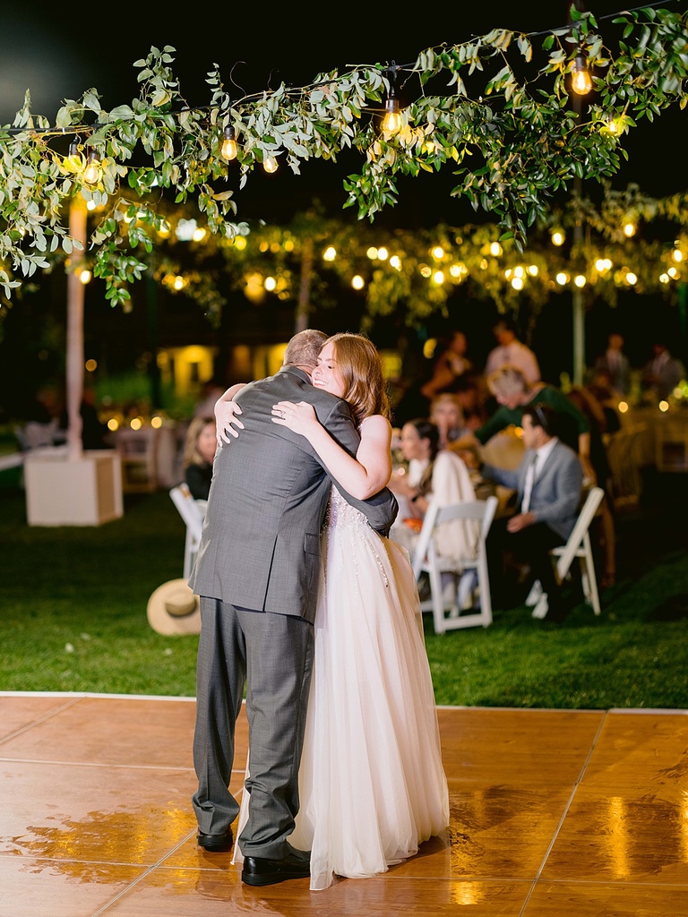 A bride and father hugging after a father-daughter dance at an outdoor reception at night.