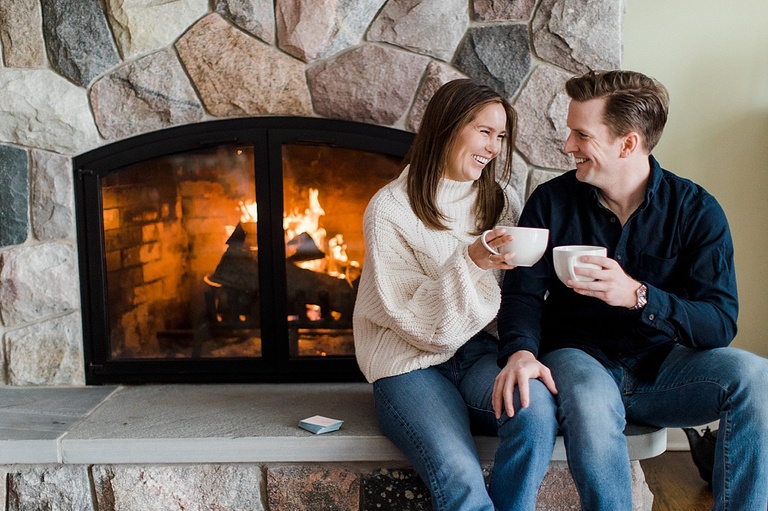 An engaged couple sitting by a fire drinking hot chocolate in Cheboygan, Michigan