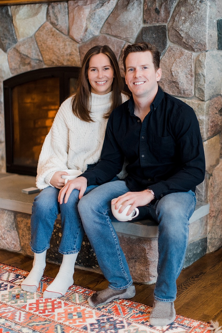 A couple taking engagement photos by a fireplace in the winter in Northern Michigan