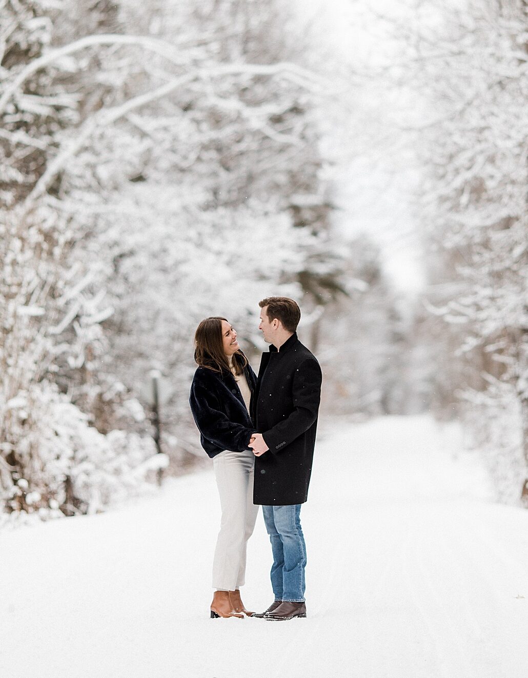 A couple smiling at each other and holding hands on a snowy covered trail