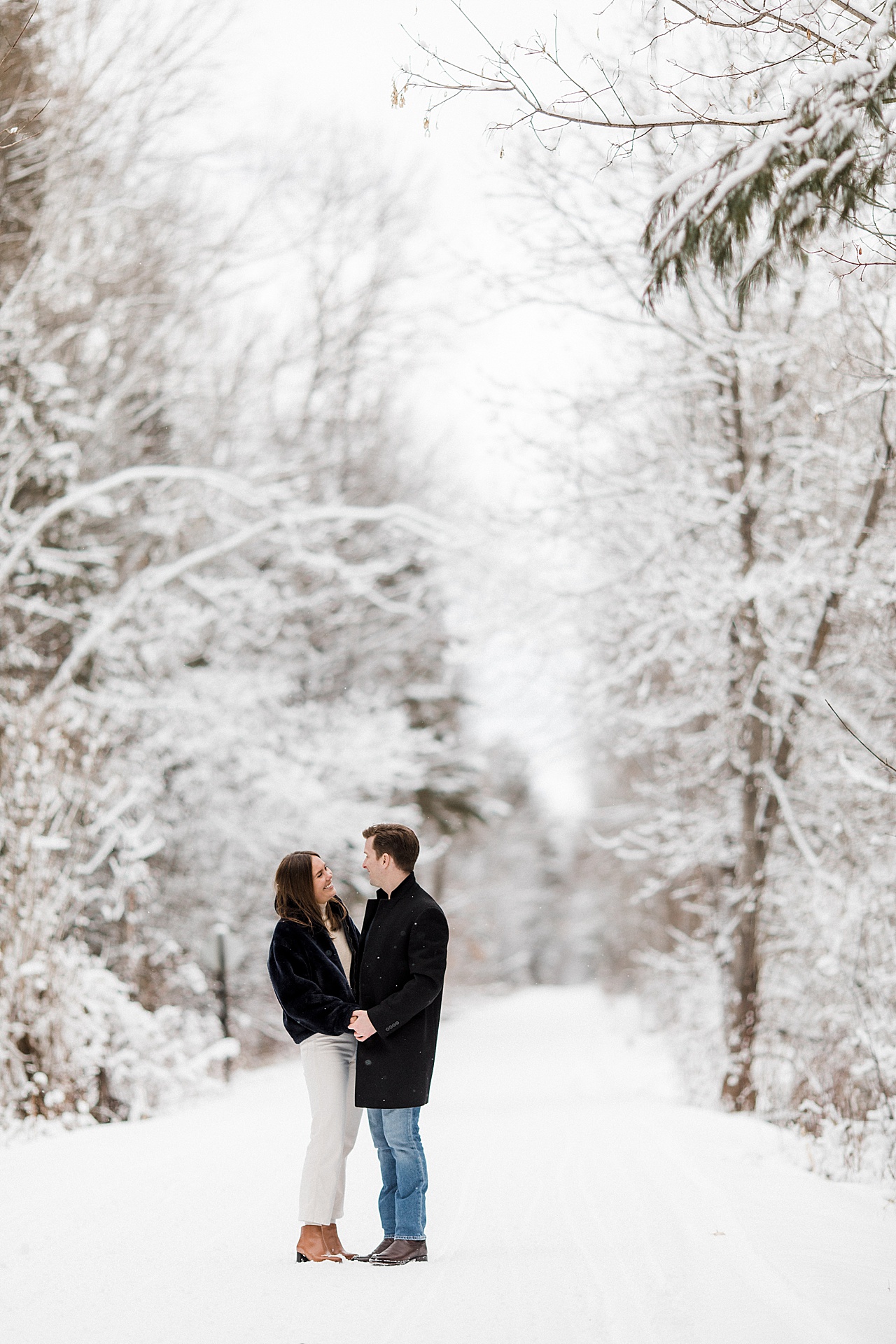 A couple smiling at each other and holding hands on a snowy covered trail