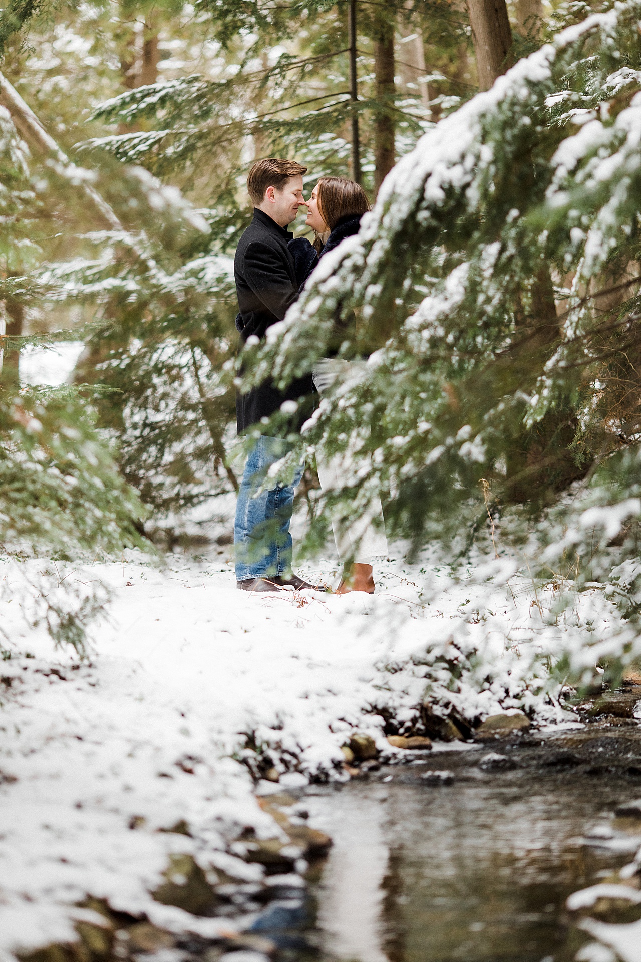 An engaged couple taking portraits by a snowy creek in Mullett Lake, Michigan