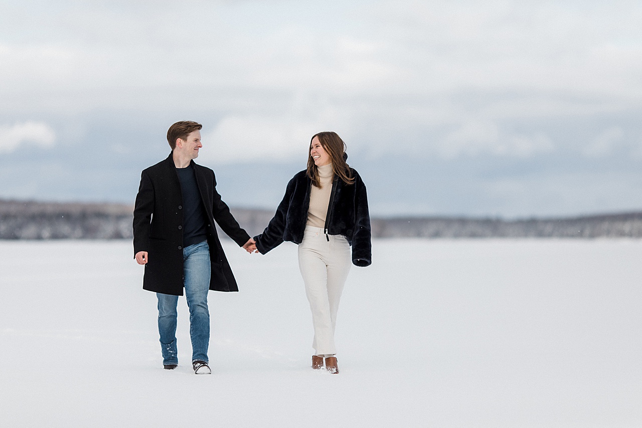 A couple walking hand in hand and smiling at each other on a frozen lake in the winter in Michigan