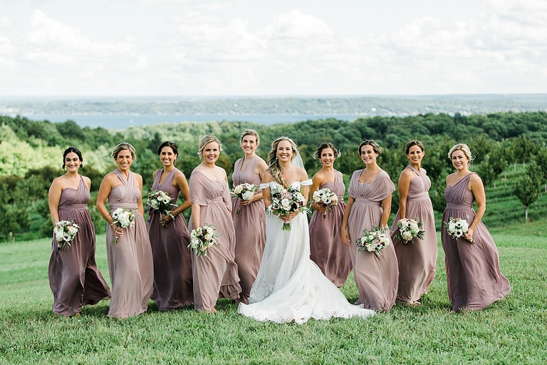 A bride and bridesmaids that are wearing mauve dresses taking portraits Bay View Weddings at Gallagher Farms