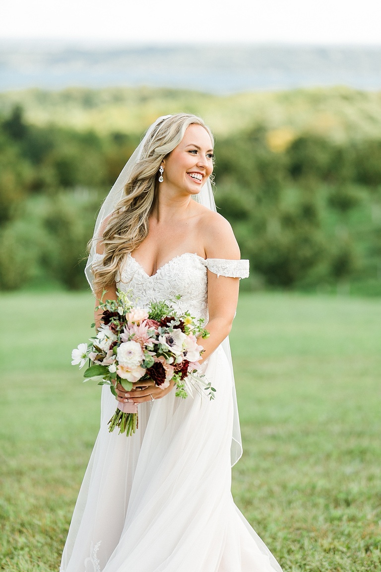 A bride smiling while taking portraits on a grassy bluff overlooking Grand Traverse Bay