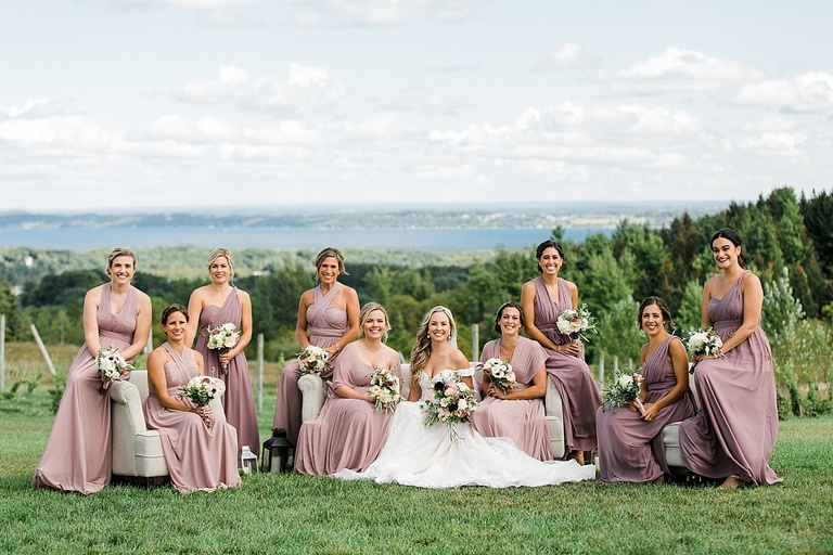 A bride and bridesmaids sitting on couches on a grassy bluff that overlooks Lake Leelanau and Grand Traverse Bay