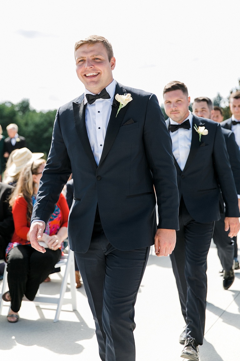 A groom smiling as he walks down the aisle to the from of the ceremony