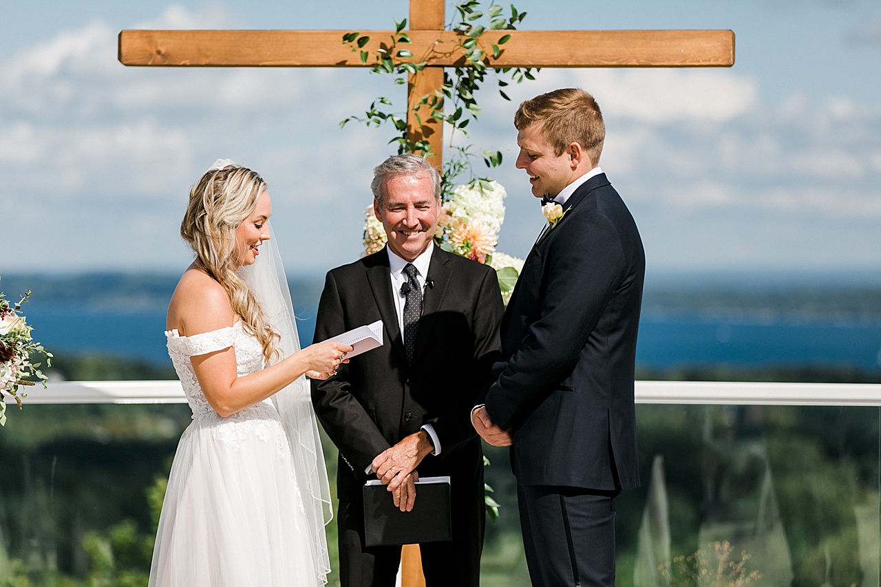 A bride reading her vows with a blue lake in the background on a sunny day on Leelanau Peninsula