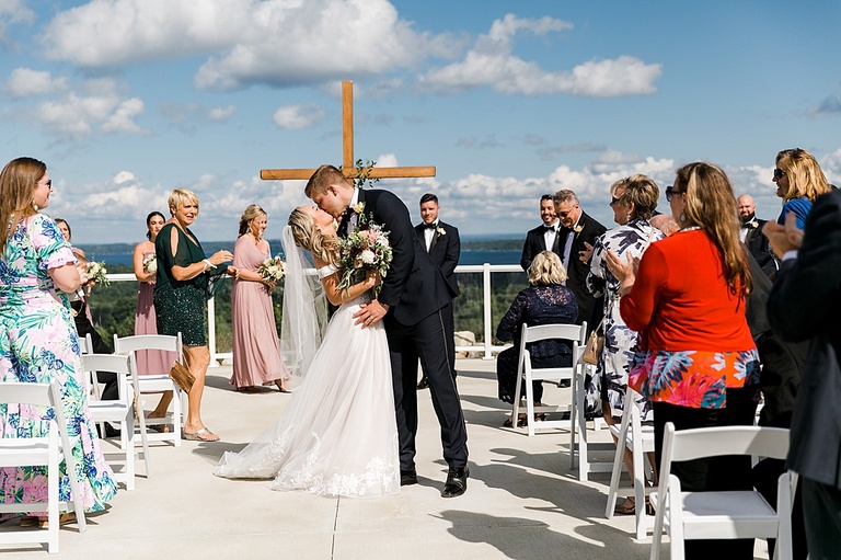 A bride and groom kissing while all their guests clap and cheer on a sunny day with blue skies in Traverse City, Michigan