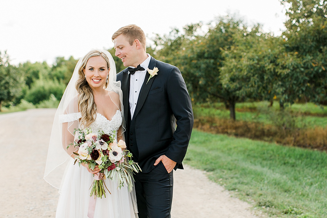 A bride smiling at the camera while her husband looks at her
