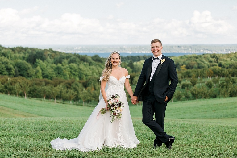 A bride and groom holding hands and smiling with Traverse City, Michigan in the background