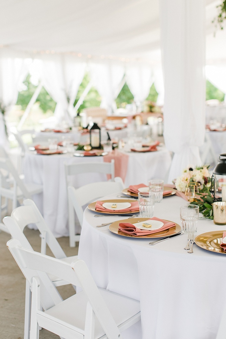 Round reception tables with white table cloths, gold chargers, and pink napkins