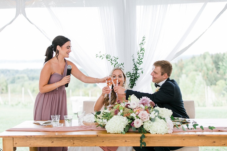 A bride and groom clinking their champagne glasses with a bridesmaid after her toast