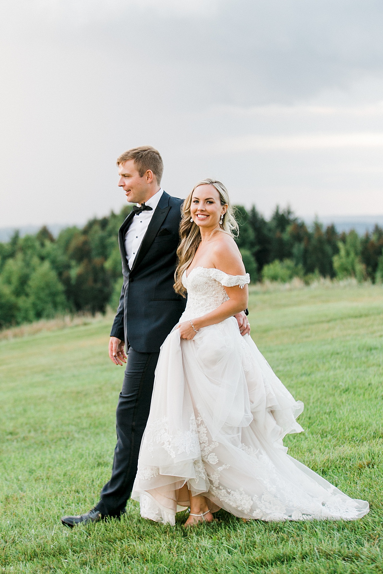 A bride walking and smiling with her husband at sunset in Northern Michigan at Bay View Weddings at Gallagher Farms