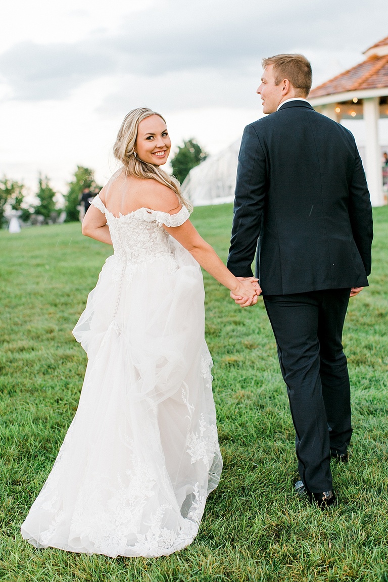 A bride looking back at the camera and smiling while walking toward the reception with her husband