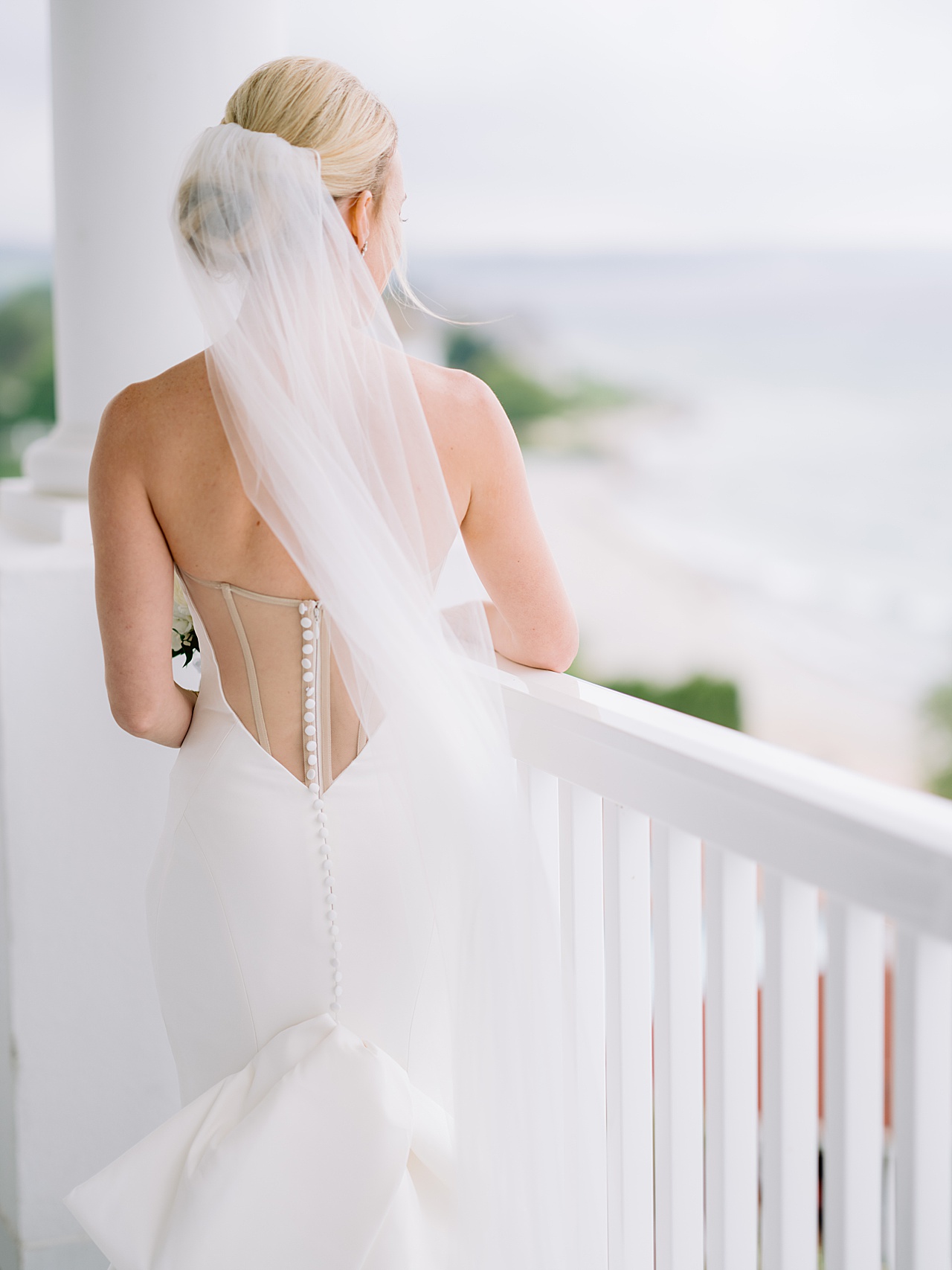 A photograph of a bride looking out from a balcony while the Michigan breeze blows her veil