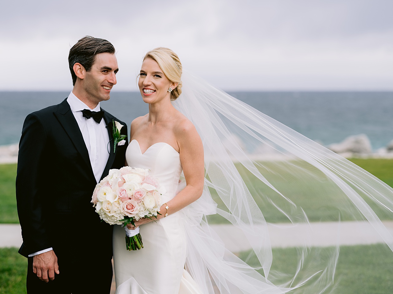 A picture of a bride and groom smiling as the wind blows the bride's veil