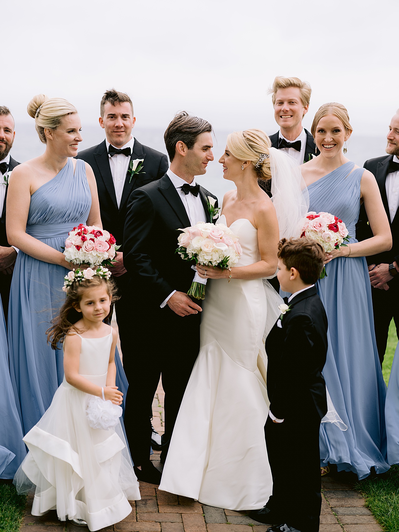 A bride and groom look at each other and smile with the wedding party around them