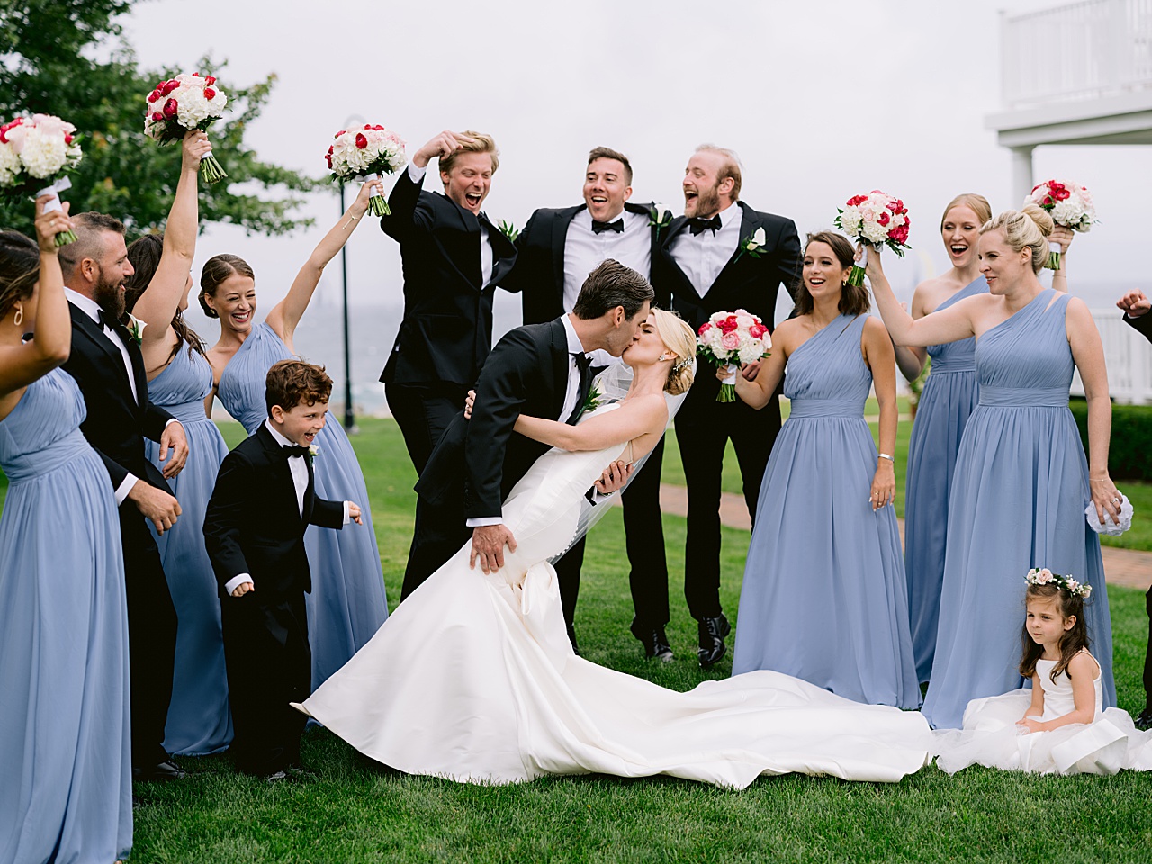 A picture of a groom dipping the bride and kissing her while the wedding party looks on and cheer