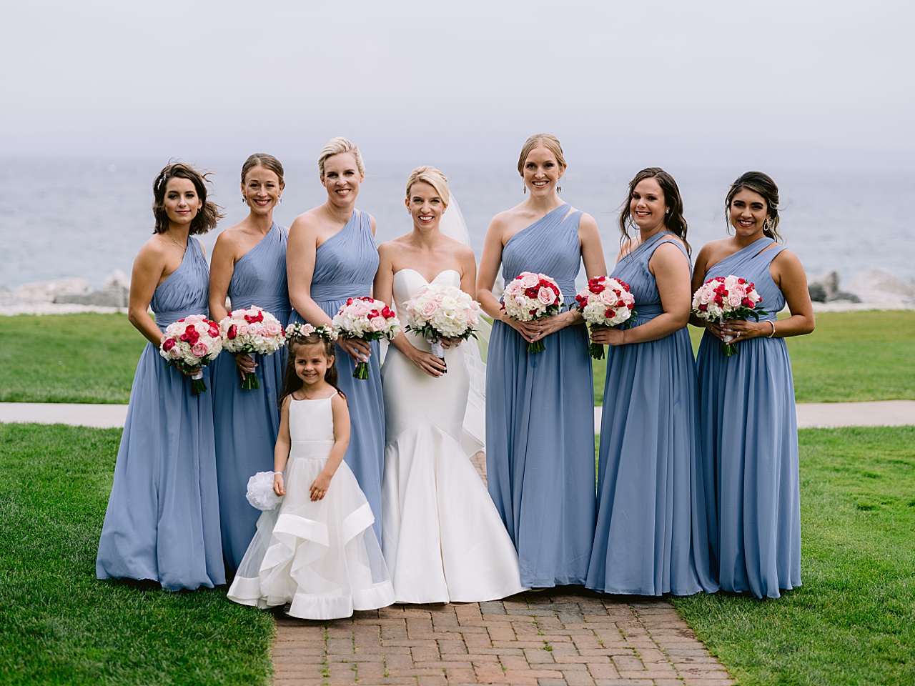 A bride smiles while surrounded by bridesmaids in blue and flower girl in Michigan