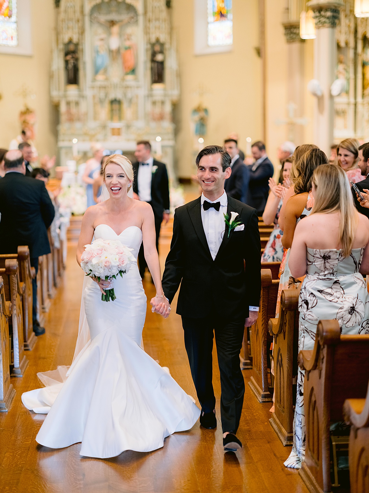 A just married bride and groom walk down an aisle together while smiling and laughing
