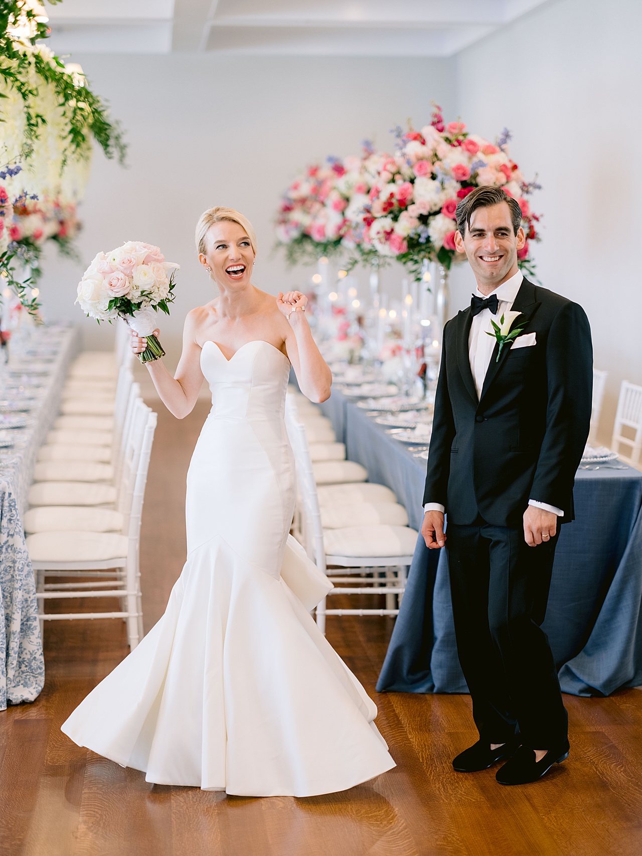 A bride and groom looking at their reception with blue table linens and tall, pink floral pieces