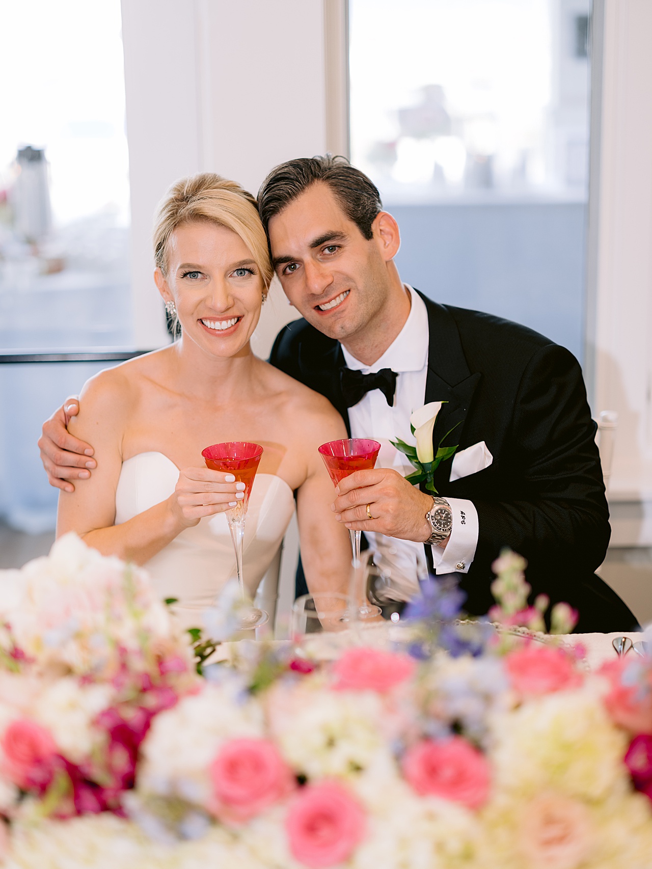 A photo of a bride and groom smiling and holding dark pink trumpet champagne flutes