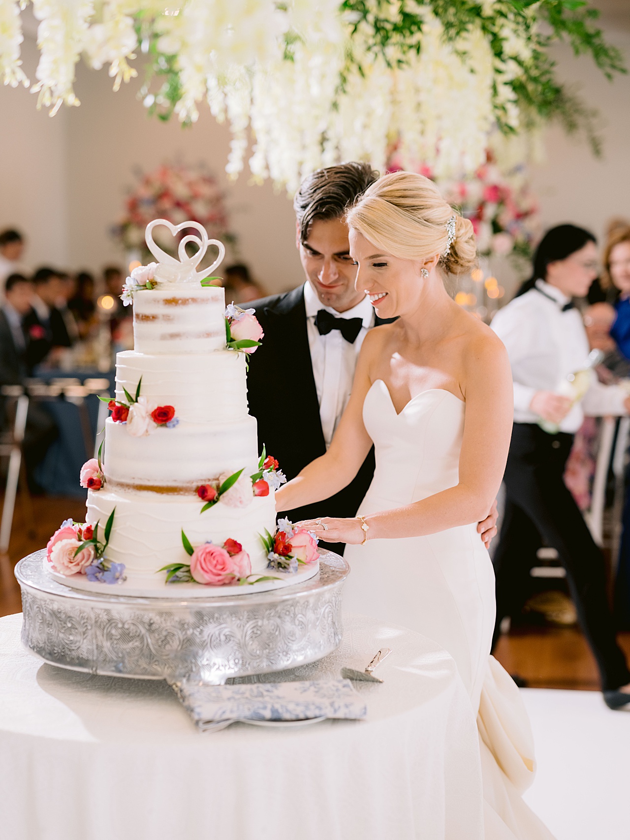 A bride and groom cutting a cake decorated with real flowers and two heart topper