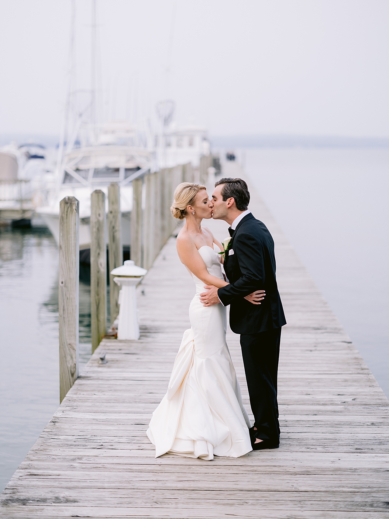 A bride and groom kissing on a misty dock on Lake Charlevoix, Michigan