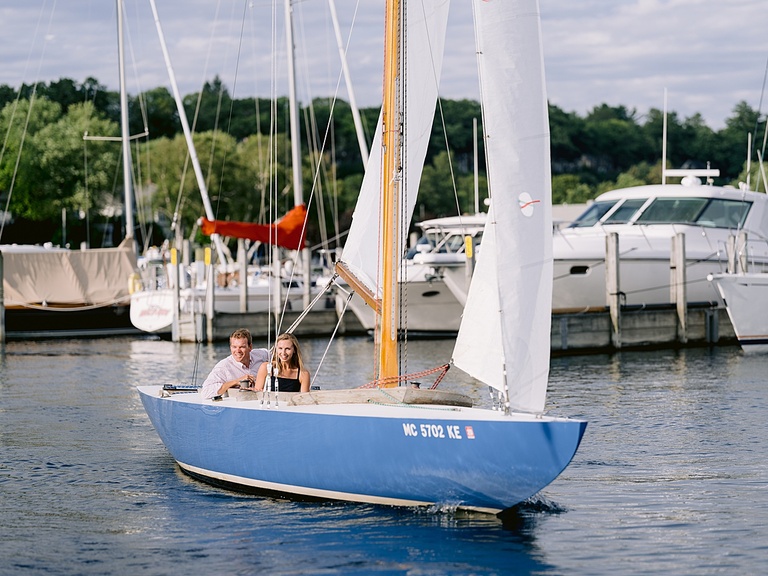 An engaged couple steering on a sailboat in Harbor Springs
