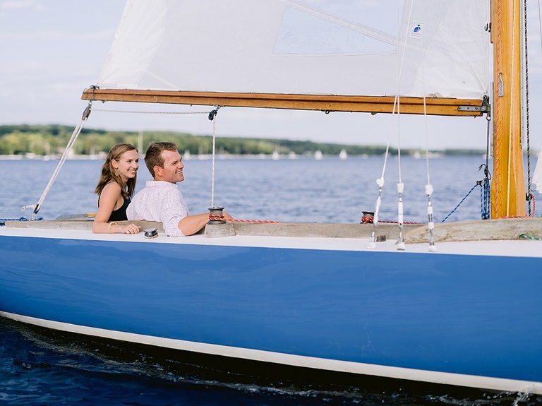 An engaged couple sitting on a sailboat and smiling on a sunny summer day