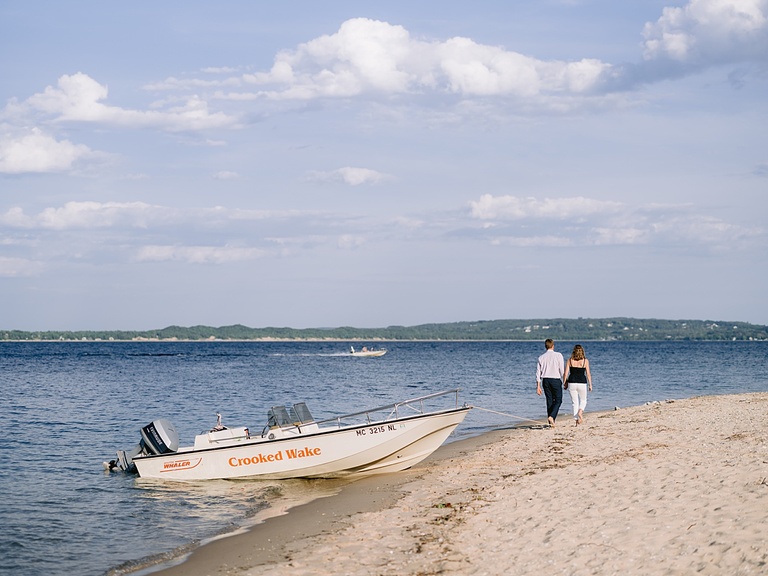 An engaged couple holding hands and walking along the beach on Harbor Point